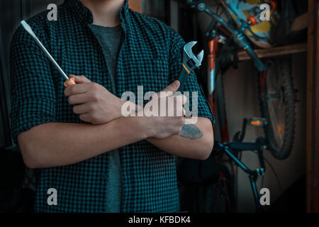 Un jeune mécanicien de classe cool avec un tatouage se préparant à fixer des vélos avec des outils Banque D'Images