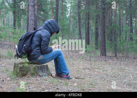 Une femme assise sur une souche dans les bois tôt le matin et vérifie son portable. Un female hiker, backpacker trekking dans les bois et les montagnes. H Banque D'Images