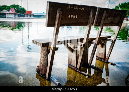 Vieux banc en bois installé sur le sol en ciment dans le temple après la pluie, inondé le sol. le ciel est lumineux après la pluie. Banque D'Images