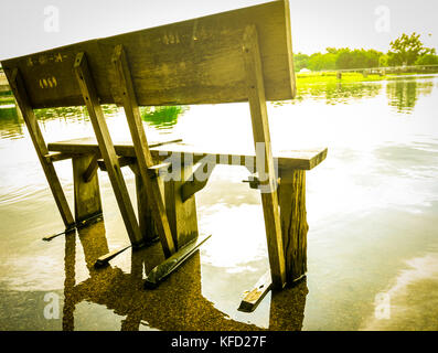 Ancien banc en bois installé sur le sol en ciment après la pluie, inondé le sol. Le ciel est brillant après la pluie. Banque D'Images