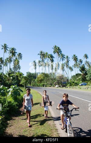 Moorea, Polynésie française. Les enfants de la planche à roulettes et le vélo. Banque D'Images