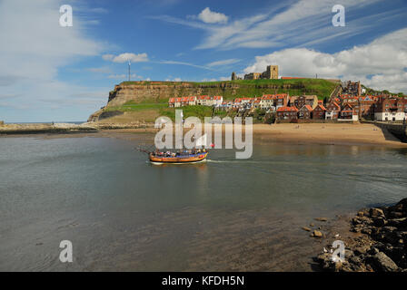 L'abbaye de Whitby et l'église St Mary sur la falaise est, vue de l'autre côté de l'entrée du port, tandis qu'un bateau touristique part. Banque D'Images