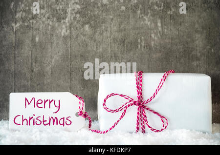 Un cadeau blanc avec étiquette avec le texte anglais joyeux Noël. gris ciment grunge background avec la neige. Banque D'Images