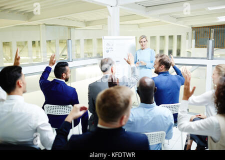 Les accompagnateurs de séminaire d'entreprise lèvent la main pour répondre à coach question après la présentation Banque D'Images