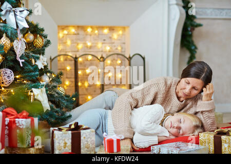 Fatigué girl sleeping sur le plancher entre les boîtes-cadeaux avec sa grand-mère située près de par Banque D'Images
