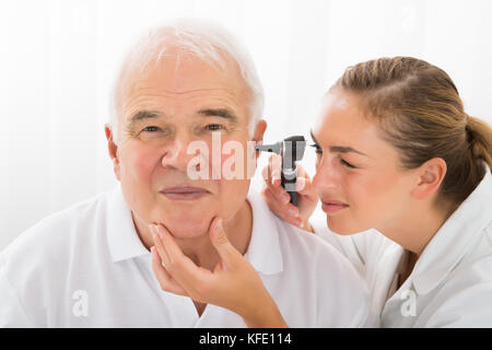 Jeune femme médecin regardant senior male patient grâce à l'oreille d'un otoscope Banque D'Images