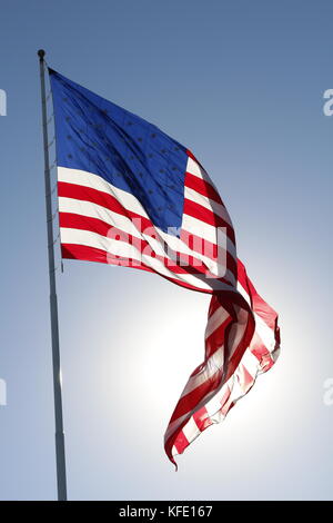 L'American flag flying fier contre le soleil dans un ciel bleu clair. Banque D'Images