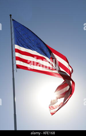 L'American flag flying fier contre le soleil dans un ciel bleu clair. Banque D'Images