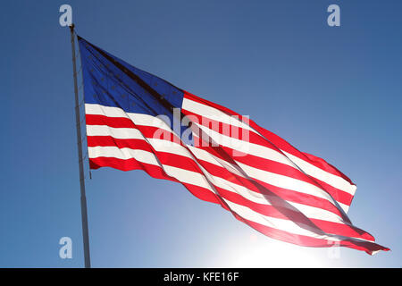 L'American flag flying fier contre le soleil dans un ciel bleu clair. Banque D'Images