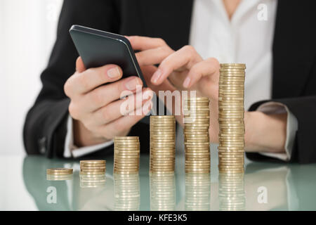 Close-up of businesswoman using smartphone avec pièces empilées sur 24 Banque D'Images