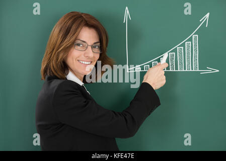 Portrait of young female teacher holding chalk in classroom Banque D'Images