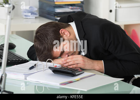 Jeune homme dormir avec les factures sur desk in office Banque D'Images