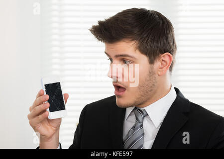 Malheureux jeune businessman looking at mobile phone in office cassé Banque D'Images