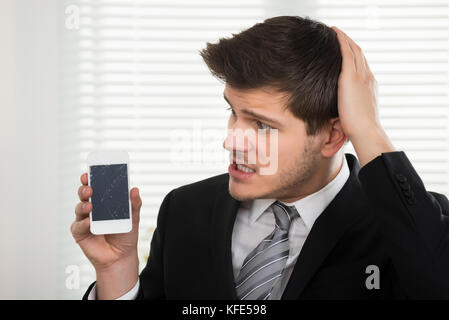 Malheureux jeune businessman looking at mobile phone in office cassé Banque D'Images