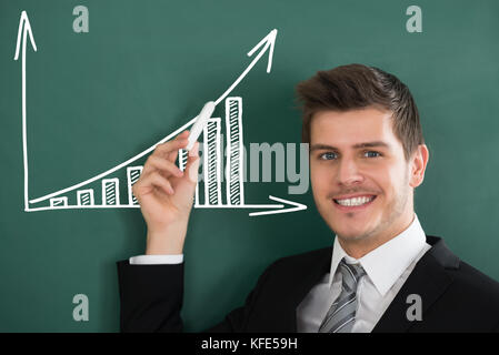 Young happy businessman holding blackboard chalk face de graphique montrant Banque D'Images