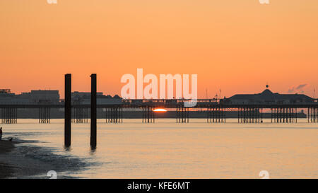 Un homme avec un chien regarde le soleil apparaître sur l'horizon derrière le Palace Pier, Brighton, Royaume-Uni Banque D'Images