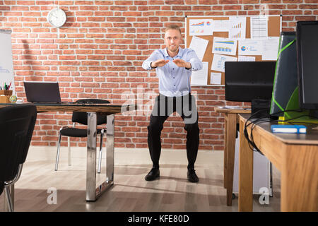 Happy businessman doing exercise in front of computer at office Banque D'Images