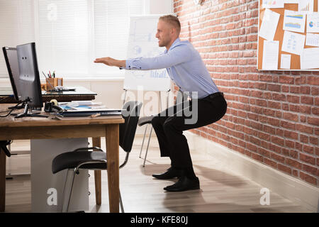 Happy businessman doing exercise in front of computer at office Banque D'Images