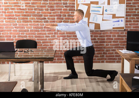 Attractive businessman doing exercise in office against brick wall Banque D'Images