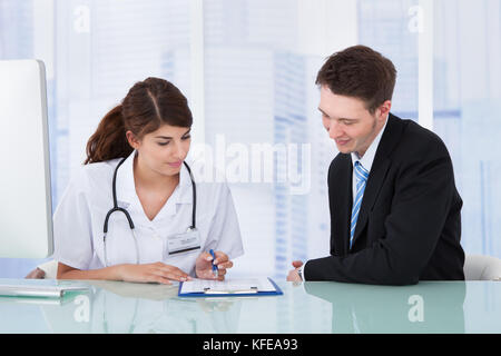 Jeune femme médecin montrant un rapport à businessman in clinic Banque D'Images