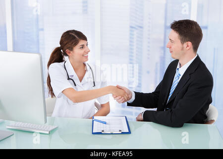 Jeune femme médecin greeting businessman at desk in clinic Banque D'Images