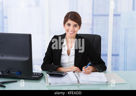 Portrait of young businesswoman using calculator at office desk Banque D'Images