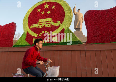 Un Chinois monte un location passé un énorme monument de Mao Zedong à Kashgar, ville de la région autonome Uygur du Xinjiang de Chine Banque D'Images