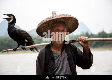 Un vieux pêcheur se prépare pour la pêche d'une manière traditionnelle en utilisant part cormorant dans l'arrière-plan de montagnes dans la province de Guangxi Banque D'Images