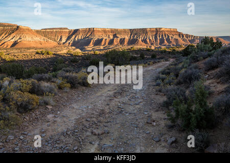 Un chemin de terre rocailleux serpente à travers le désert de l'Utah du sud, que le soleil s'affaiblit et lumière dorée ajoute un éclat à l'orange et rouge dans l'isolation partiellechauffage mesas Banque D'Images