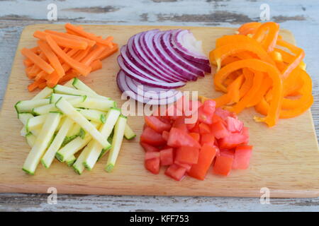 Couper en dés et les légumes sur une planche à découper en bois. l'oignon, la tomate, le paprika, la courgette, la carotte cuisine étape par étape. Banque D'Images