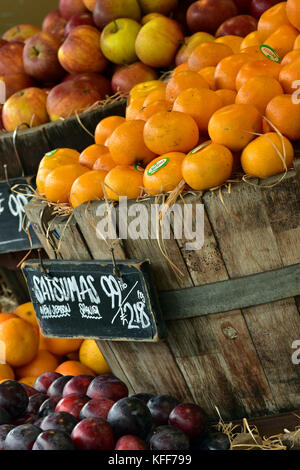 Les oranges, les pommes et les prunes à vendre empilées en vieux fûts de bois et des caisses à l'extérieur d'une boutique de légumes ou à un marché de fermiers, satsuma, clementine Banque D'Images