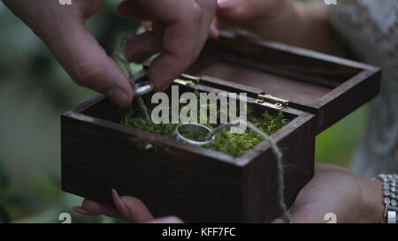 Groom tient une boîte cadeau de bijoux avec des anneaux de mariage en or. la main de l'homme prend l'anneau de mariage de la boîte en bois Banque D'Images
