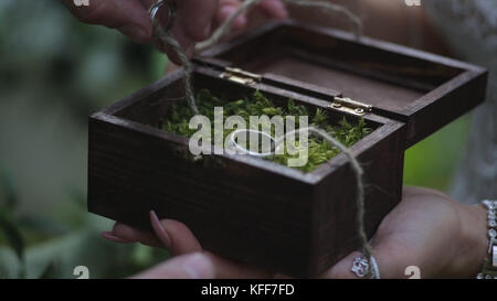 Groom tient une boîte cadeau de bijoux avec des anneaux de mariage en or. la main de l'homme prend l'anneau de mariage de la boîte en bois Banque D'Images