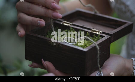 Groom tient une boîte cadeau de bijoux avec des anneaux de mariage en or. la main de l'homme prend l'anneau de mariage de la boîte en bois Banque D'Images