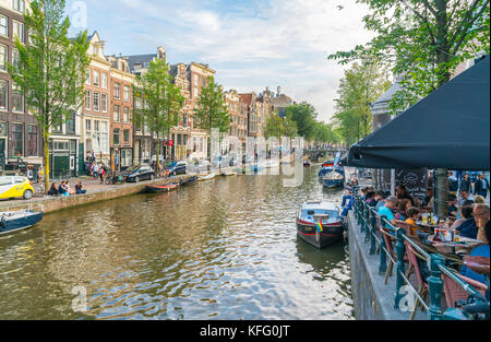 Amsterdam, Pays-Bas - le 17 août 2017 ; les gens se détendre en fin de journée assis aux côtés de canal et de cafés au bord du canal avec bords amarrés sur offrent la garantie de tr Banque D'Images