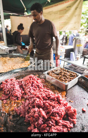 Un homme cuit viande sur un grill géant dans les marchés de l'arrondissement, Londres, Angleterre Banque D'Images