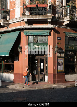 Femme marche sur trottoir en fin d'après-midi on cell phone in front of old green et brown bar de San Telmo domaine de Bueno Aires, Argetina. Banque D'Images