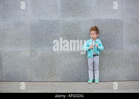 Fashion kid posant près de mur gris Banque D'Images