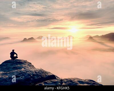 Moment de solitude sur le sommet rocheux exposés. man in black profitez d'une vue merveilleuse. s'asseoir sur le randonneur pic de roche et de regarder dans la brume et le brouillard coloré Banque D'Images
