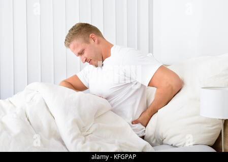 Portrait de jeune homme assis sur le lit de souffrance backpain Banque D'Images