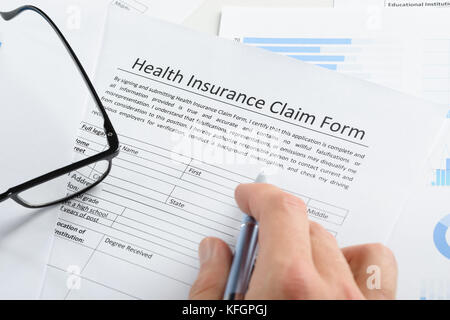 Gros plan sur le formulaire de demande de remboursement d'assurance maladie de la main tenant le stylo Banque D'Images