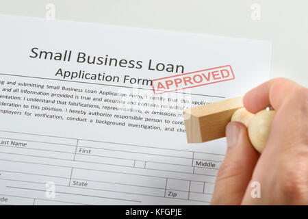 Gros plan de la personne tenant la main du tampon en caoutchouc approuvé sur le formulaire de demande de prêt Banque D'Images