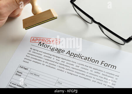 Gros plan de la main de la personne avec un tampon en caoutchouc et une marque rouge approuvée sur la demande d'hypothèque Banque D'Images