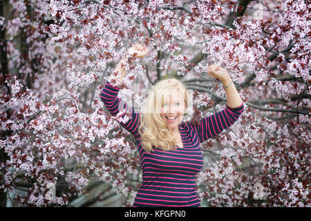 Happy smiling Caucasian woman with long hair en violet fedora hat près de blossoming cherry plum tree Banque D'Images