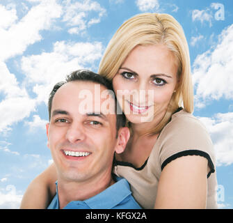 Portrait of happy Mid adult man giving piggyback ride to woman against sky Banque D'Images