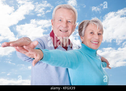 Portrait of happy senior couple with arms outstretched standing against cloudy sky Banque D'Images