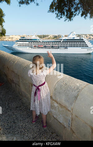 Malte, en jardins Barrakka, une petite fille de 7 ans dit au revoir / adieu à bateau de croisière qui navigue sur le Grand Port. (91) Banque D'Images