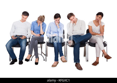 Il y a plein de gens d'affaires qui s'ennuient assis sur des chaises sur fond blanc Banque D'Images
