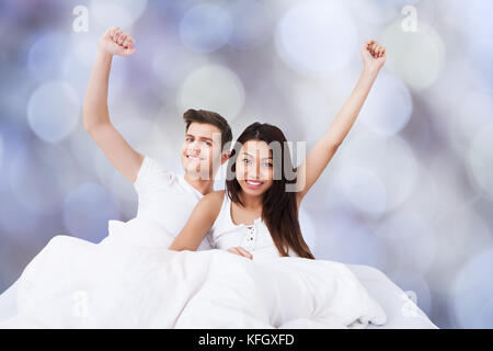 Portrait d'un couple multiethnique réussi avec les bras levés sur le lit Banque D'Images