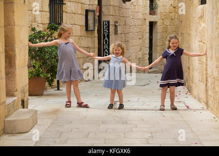 Trois jeunes sœurs / filles / Enfants / Enfants / enfant âgés de 7, 3 et 5 ans, sur des vacances en famille, jouer et courir et span une rue étroite à Mdina, Malte Banque D'Images